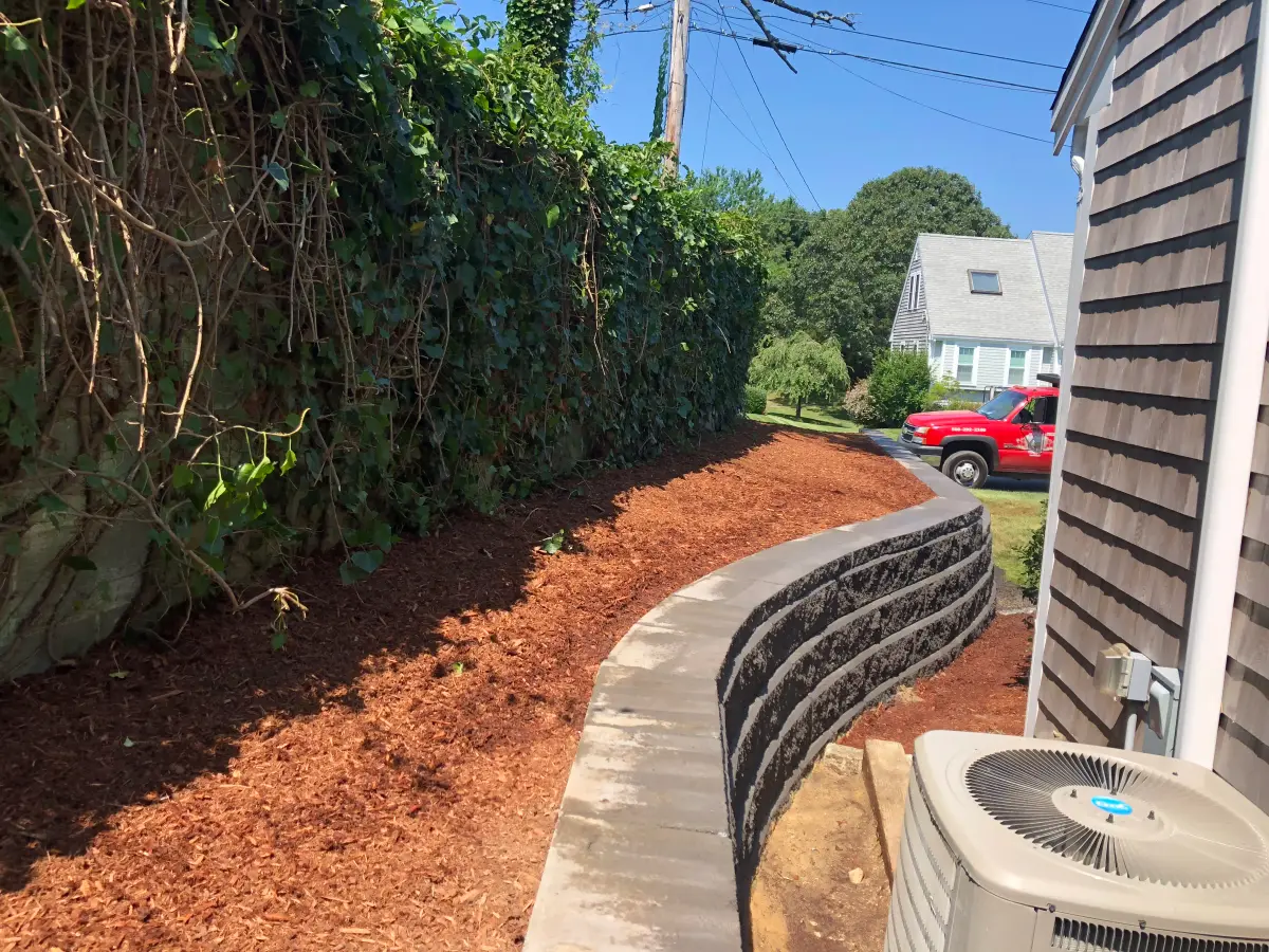 Curved charcoal block retaining wall following a side yard grade change in Centerville, MA by Braun Construction