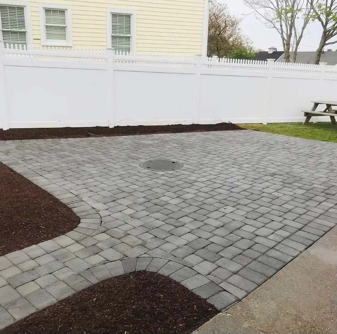Gray paver patio with a contrasting cobblestone border and curved walkway built by Braun Construction on Cape Cod