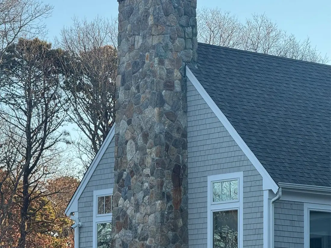 Shingled home with a fieldstone chimney and white picket fence completed by Braun Construction in Massachusetts